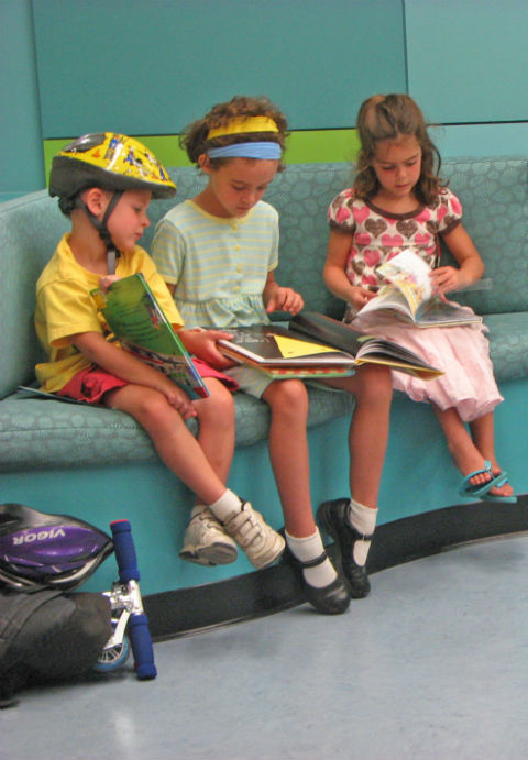 Three children sitting on a couch in the library reading books